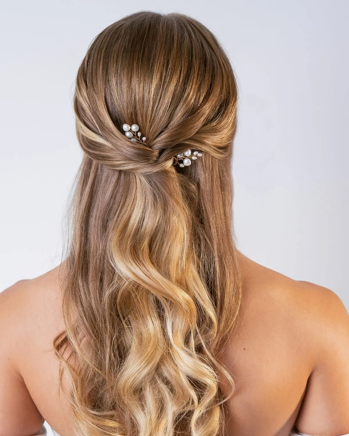 Rückansicht einer Braut mit blonden, gewellten Haaren im Half-up-Styling, verziert mit den goldfarbenen Perlen-Haarnadeln Leonie von Sternenauge
