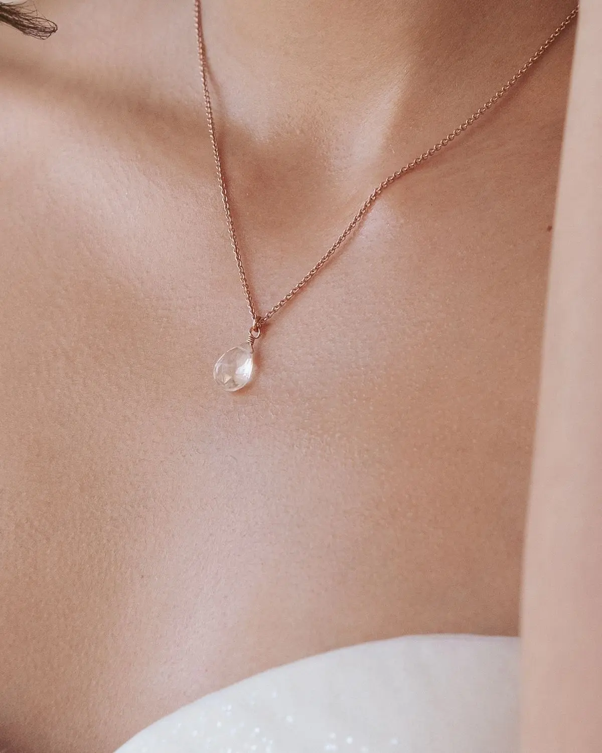 Nahaufnahme der Sternenauge Halskette Kyra in Roségold mit Tropfenanhänger, präsentiert zum weißen Brautkleid am Dekolleté