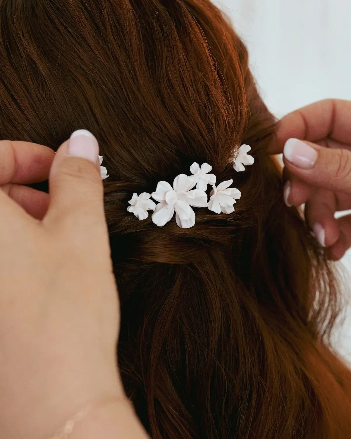 Handgefertigter Brauthaarschmuck VALERIA von Sternenauge: Drei Haarnadeln mit matten, weißen Blütenelementen werden als filigranes Bouquet in die Frisur einer Braut mit kastanienbraunem Haar eingearbeitet.