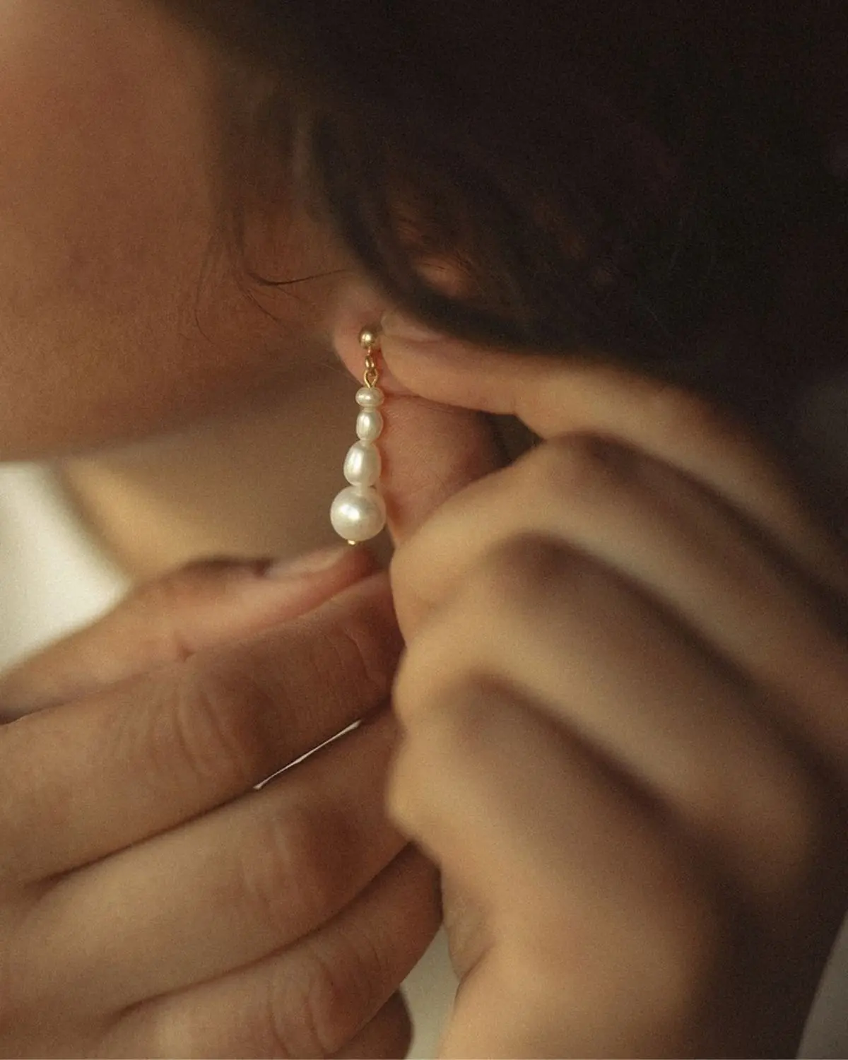 Detailaufnahme der goldenen Sternenauge Nora Ohrringe aus 925 Sterling Silber mit 18k Vergoldung und Süßwasser-Zuchtperlen, die am Ohr angelegt werden.