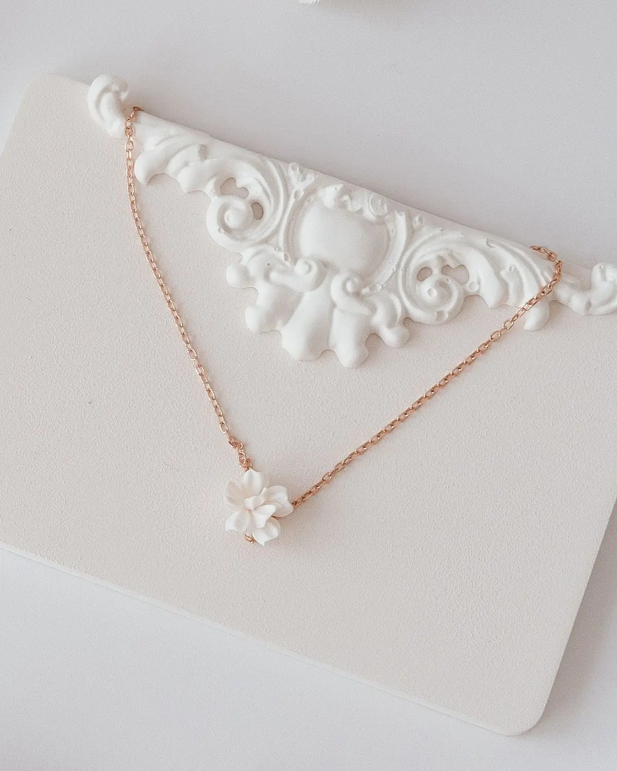 Filigrane Sternenauge Halskette Valeria aus 18k rosévergoldetem 925 Sterling Silber mit einem detailreichen, dreidimensionalen weißen Blütenanhänger, elegant arrangiert auf einem hellen Hintergrund mit Stuck-Element.
