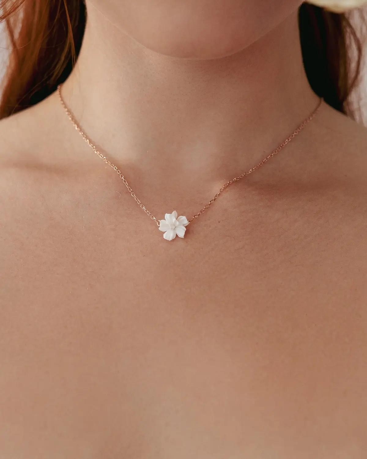 Nahaufnahme der getragenen Sternenauge Halskette Valeria am Dekolleté einer Braut. Die zarte Ankerkette aus 18 Karat rosévergoldetem 925 Sterling Silber liegt flach auf der Haut auf und setzt den dreidimensionalen, matt-weißen Blütenanhänger elegant in Szene.