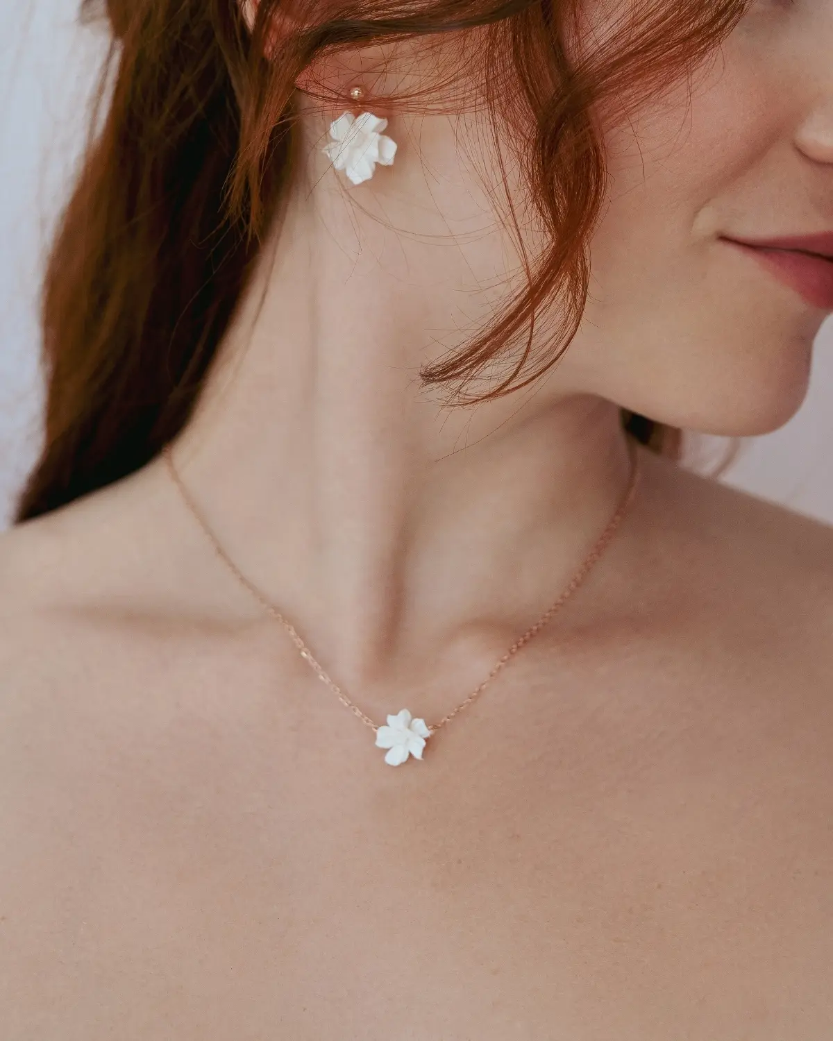 Fokussierte Nahaufnahme der getragenen Sternenauge Halskette Valeria im Zusammenspiel mit den passenden Ohrringen aus 18k rosévergoldetem 925 Sterling Silber an einer Braut. Zu sehen sind beide weißen Blütenanhänger im Detail. Styling-Beispiel – Ohrringe separat erhältlich.