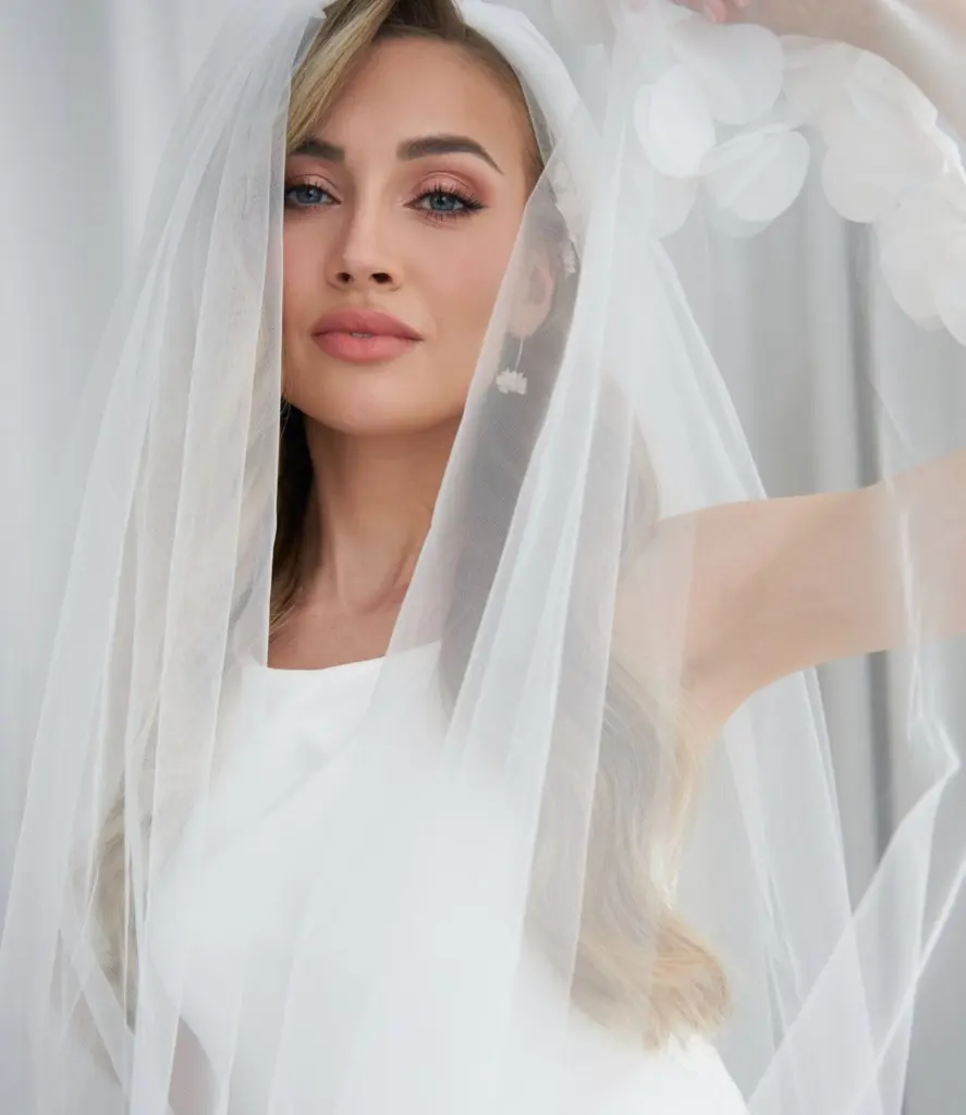 Luxuriöses Portrait einer blonden Braut aus einem Hochzeits-Styling-Workshop von Alexandra Lederer. Sie blickt durch einen feinen Tüllschleier, während die floralen Valeria Ohrhänger von Sternenauge mit ihren handgeformten weißen Blüten perfekt zur Geltung kommen.