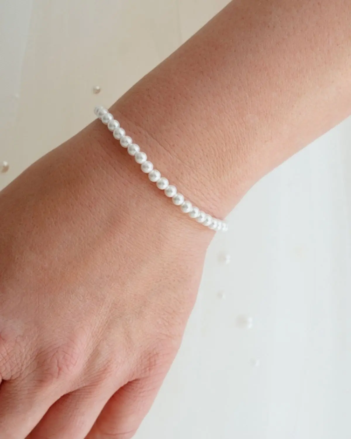 Nahaufnahme des zarten Sternenauge Annouk Armbands II aus einer Reihe 4mm kleiner Muschelkernperlen, elegant getragen an einem Handgelenk vor einem hellen, minimalistischen Hintergrund