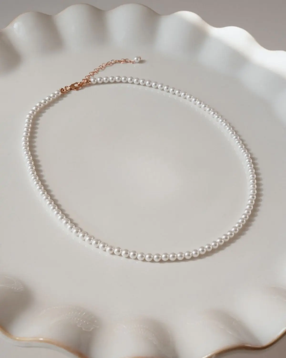 Klassische Perlenkette Annouk auf einem Keramikteller dekoriert mit Fokus auf die gleichmäßigen Muschelkernperlen und die Verlängerungskette aus 925 Sterling Silber mit 18K-Rosévergoldung