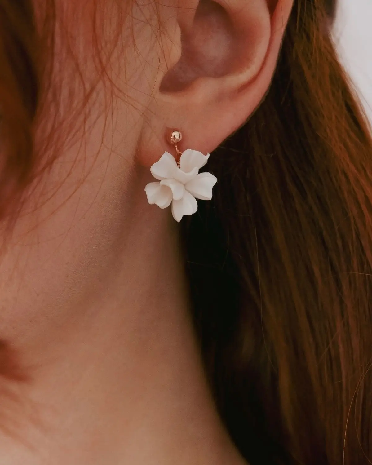 Makroaufnahme eines Brautohrrings am Ohrläppchen aus dem Valeria Schmuck-Set III für die Hochzeit von Sternenauge. Der Ohrhänger besteht aus einer filigranen, ivoryfarbenen Blüte, die an einem rosévergoldeten Kugelohrstecker aus 925 Sterling Silber befestigt ist.